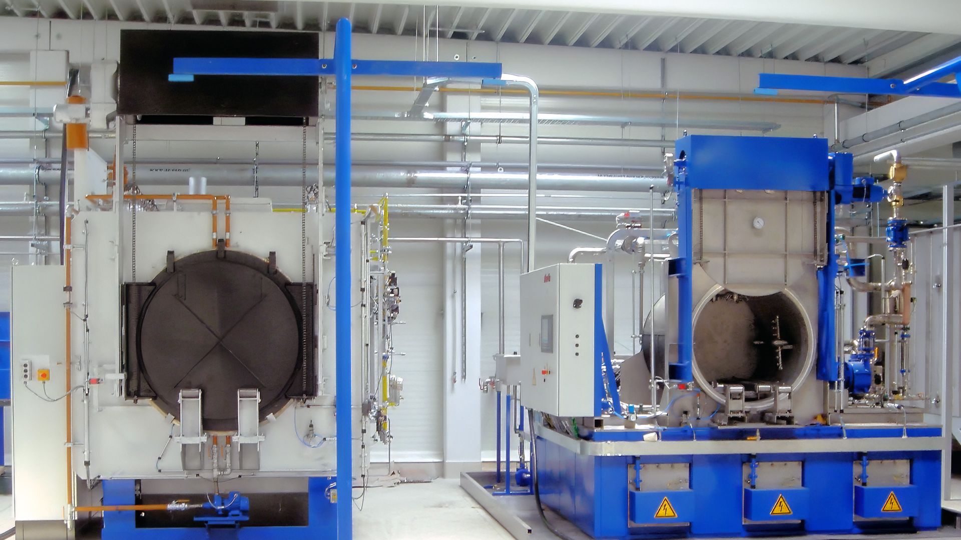 Industrial washer in a factory setting, featuring large metal equipment and various pipes, with a focus on a blue and white color scheme.