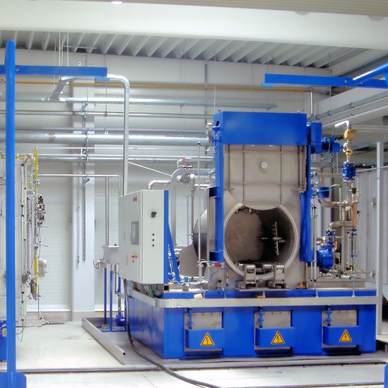 Industrial washer in a factory setting, featuring large metal equipment and various pipes, with a focus on a blue and white color scheme.