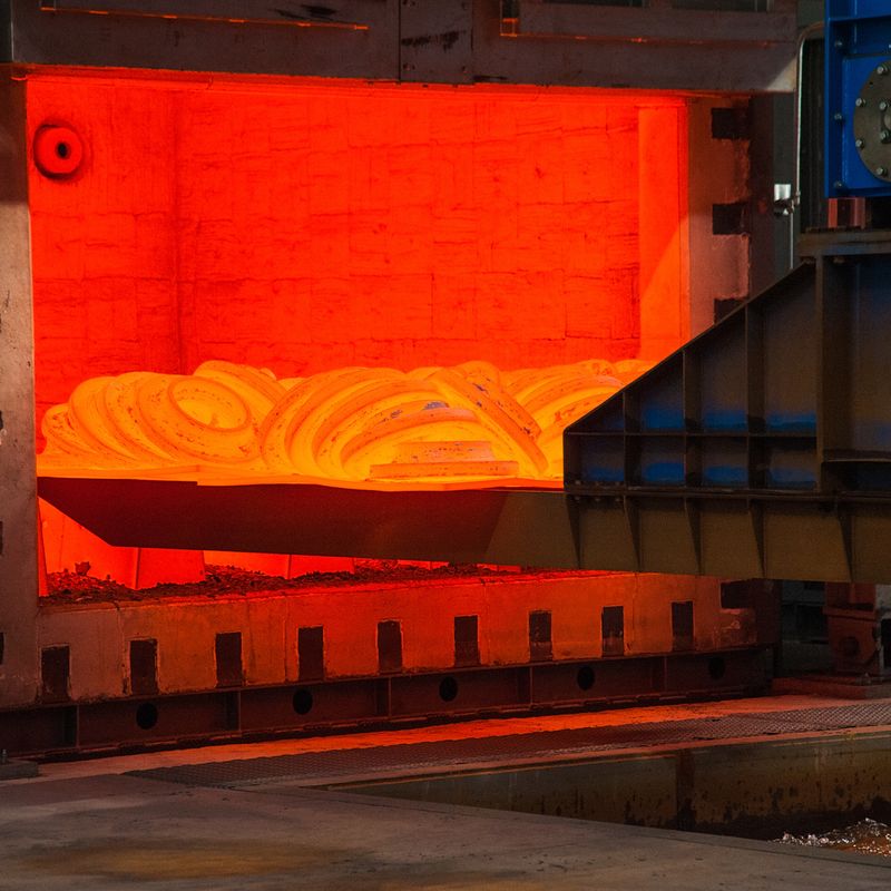 Glowing hot metal coil inside an industrial furnace, with surrounding metal structures and machinery.