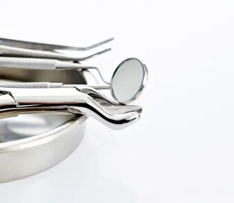 A set of shiny dental tools, including a mirror and tweezers, resting on a metal tray against a white background.