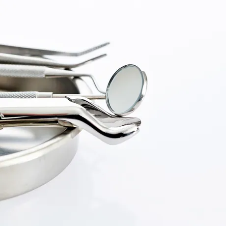 A set of shiny dental tools, including a mirror and tweezers, resting on a metal tray against a white background.