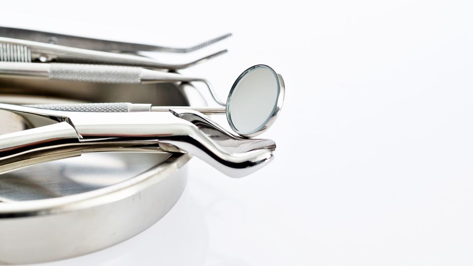 A set of shiny dental tools, including a mirror and tweezers, resting on a metal tray against a white background.